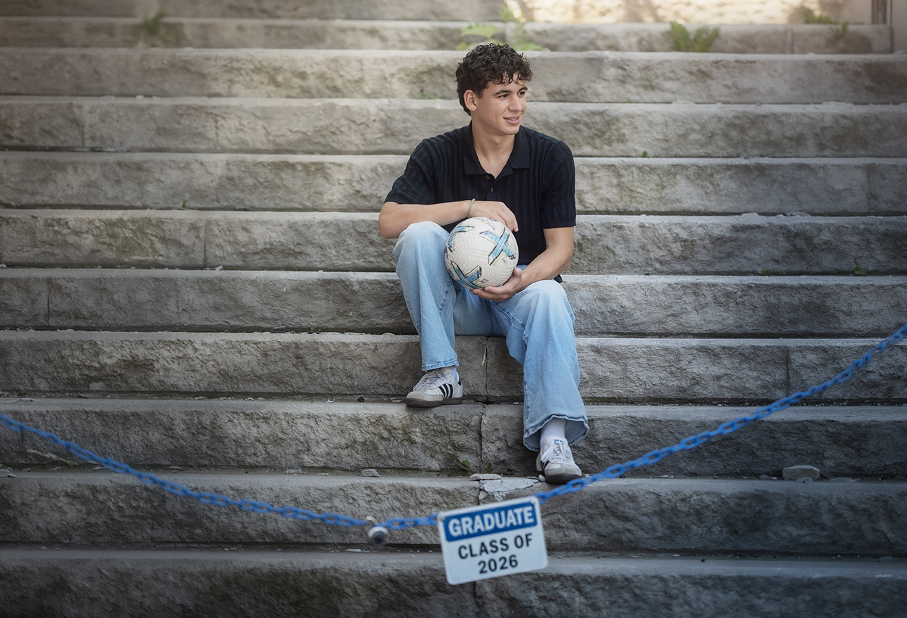 Graduate seated on school steps holding a soccer ball